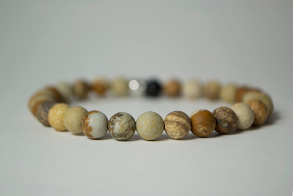 Front view of the natural stones in the Infused Picture Jasper bracelet with details of the color and texture. In the background is a blurred infusible Lava Stone bead 