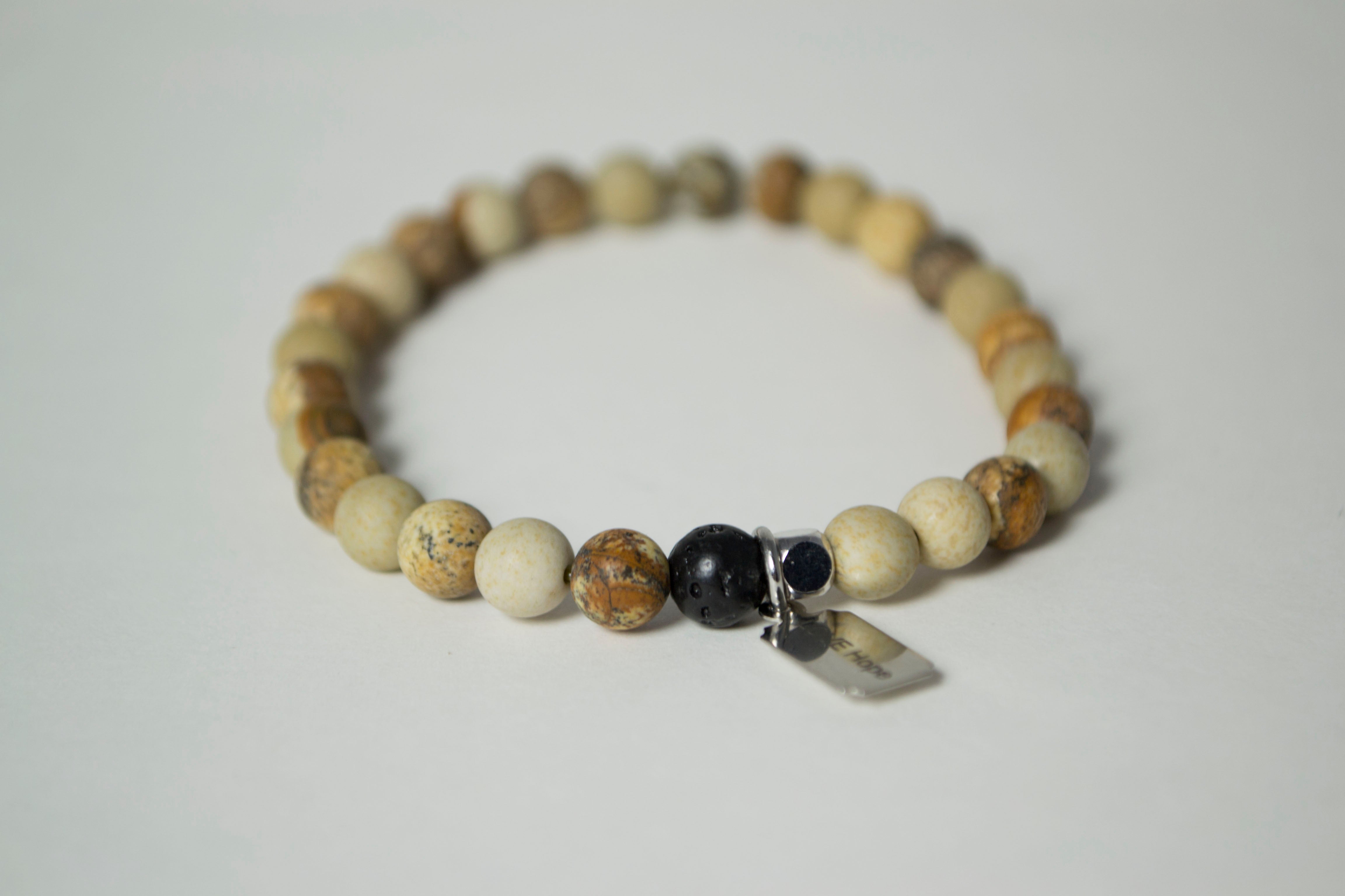 Rear view of the natural stones in the Infused Picture Jasper bracelet with details of the color and texture, including detail of the infusible Lava Stone bead. In the background is a blurred view of the front of the bracelet.