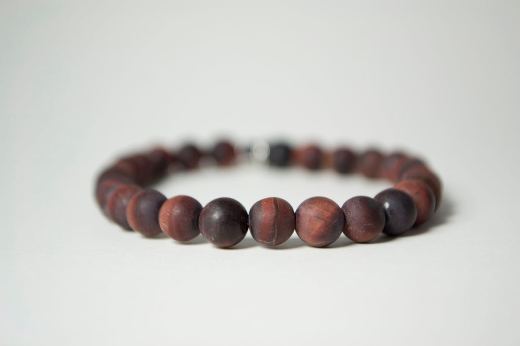 Front view of the natural stones in the Infused Red Tiger's Eye bracelet with details of the color and texture. In the background is a blurred infusible Lava Stone bead 