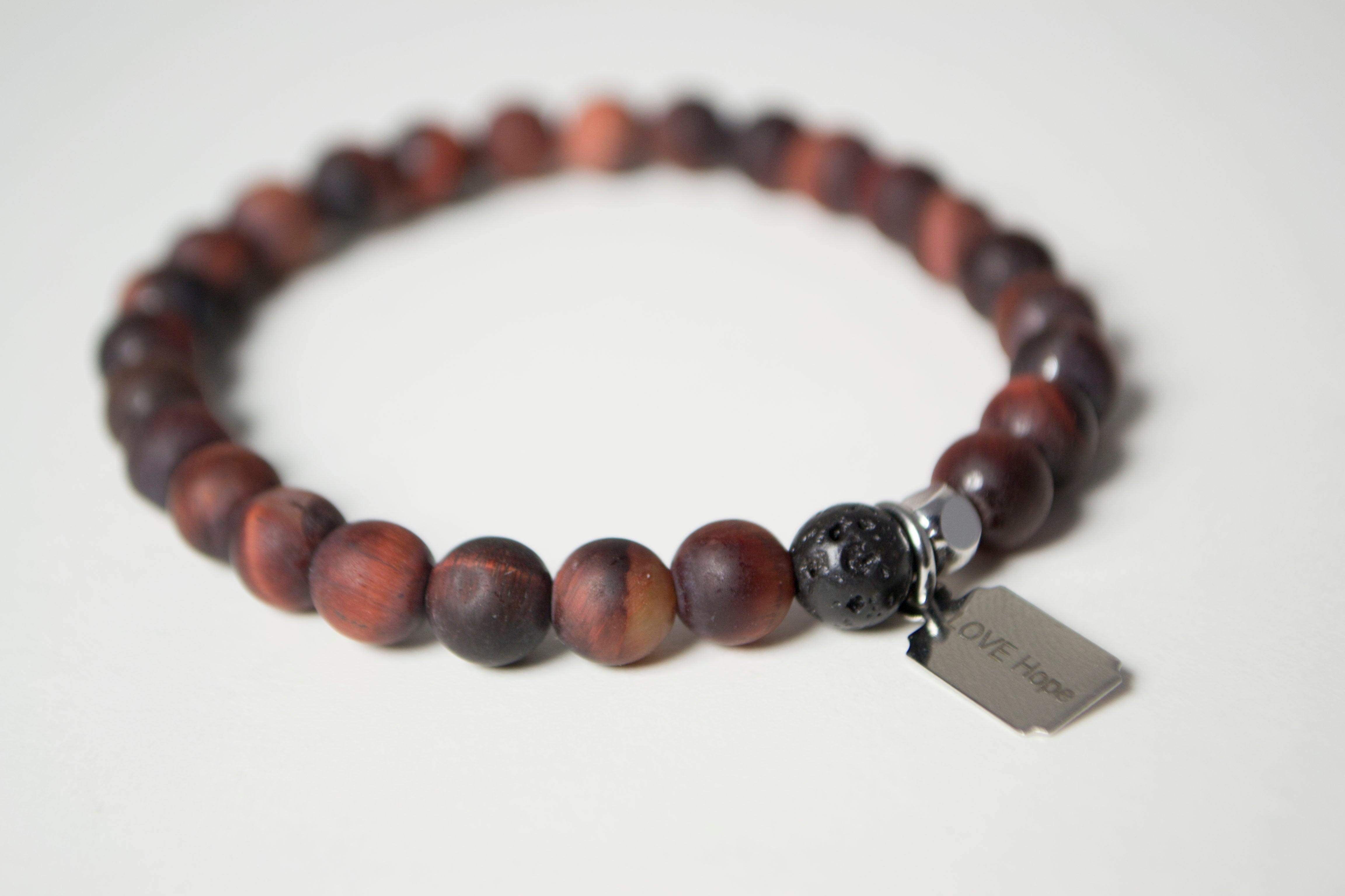 Rear view of the natural stones in the Infused Red Tiger's Eye bracelet with details of the color and texture of the infusible Lava Stone. In the background is a blurred view of the front of the bracelet